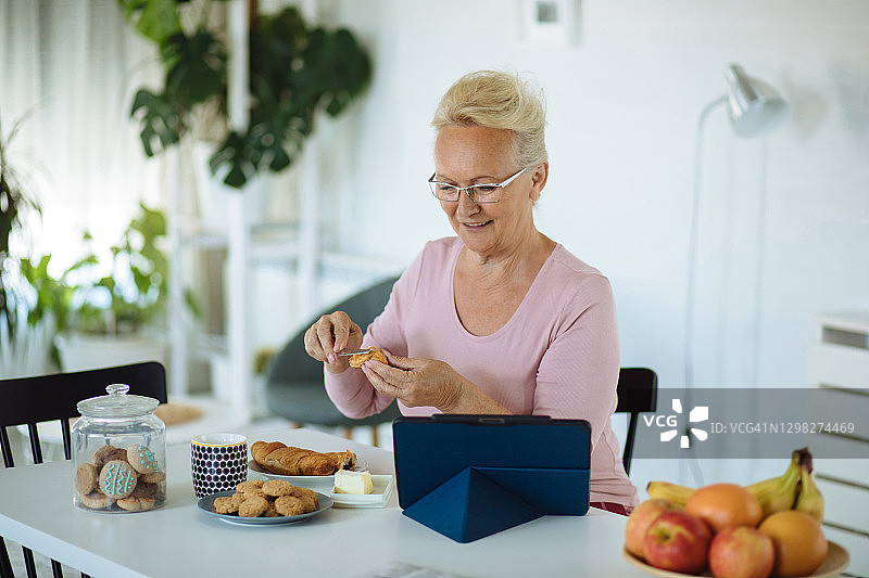 在家吃早餐时使用平板电脑的老年妇女图片素材