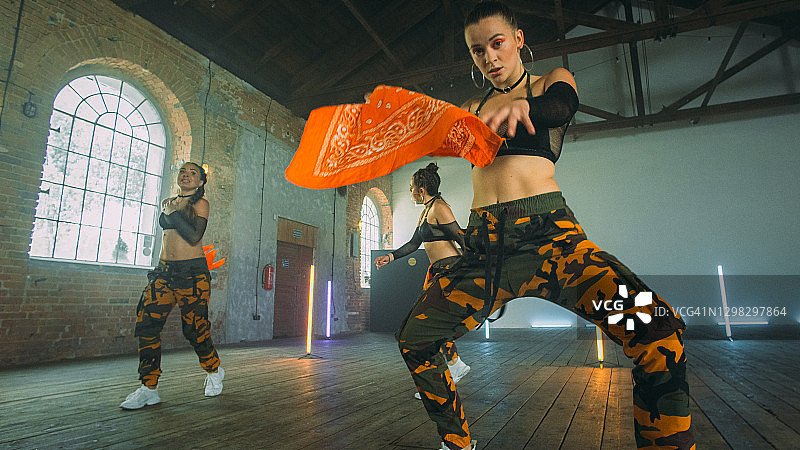 在工作室跳舞的女舞者，橙色头巾和迷彩服的舞蹈编排图片素材