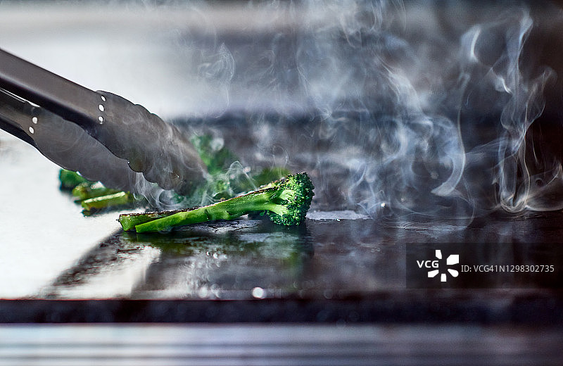 用钳子在热板上翻动新鲜西兰花图片素材