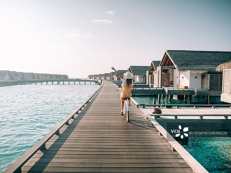 年轻女子在马尔代夫木制码头上骑自行车图片素材