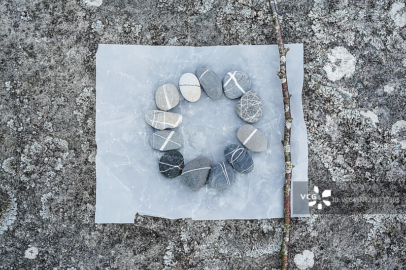 羊皮纸上12颗鹅卵石和树枝在布满地衣的岩石上排列图片素材