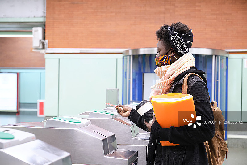 戴防护口罩的非洲女大学生在地铁站刷卡通过旋转栅门，公共交通新常态图片素材