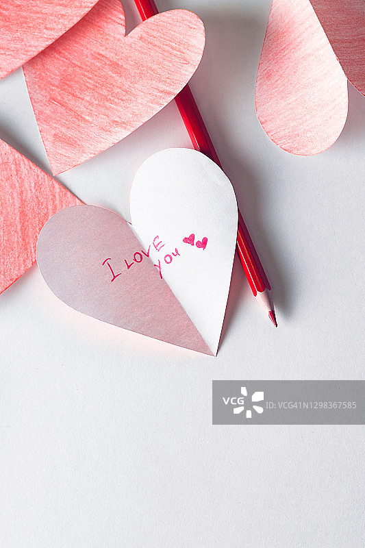 白色纸张背景上的红色情人节爱心，旁边是彩色铅笔。我爱你文字，情人节示爱概念。图片素材