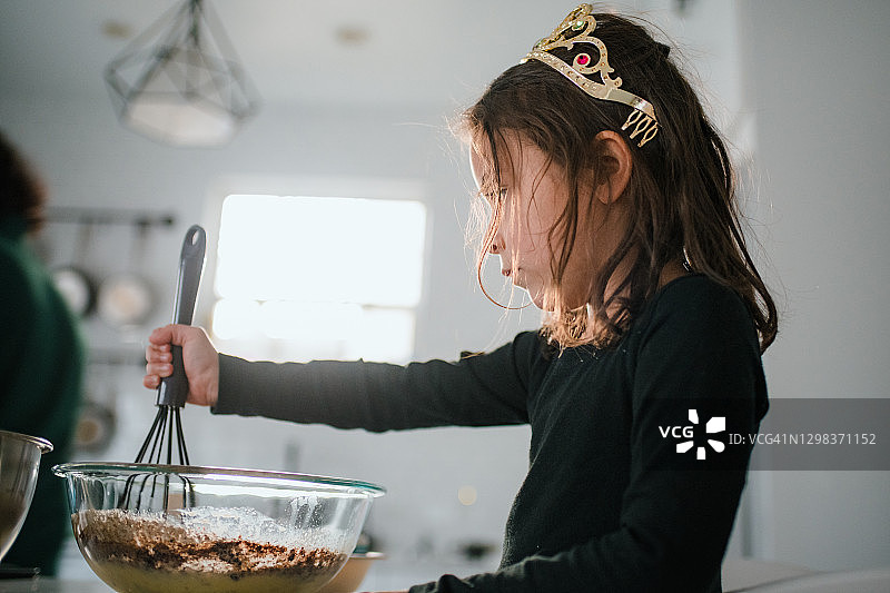 戴着头饰、用搅拌碗和搅拌器烘焙的幼儿园女孩图片素材