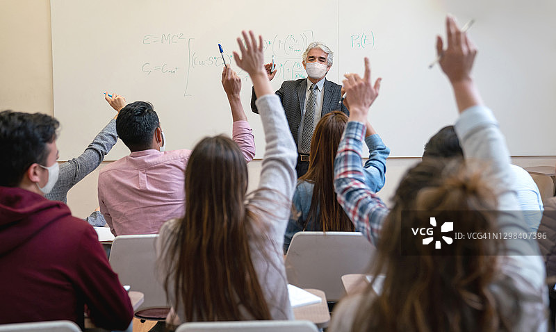 疫情期间戴口罩的老师在教室里回答学生问题图片素材