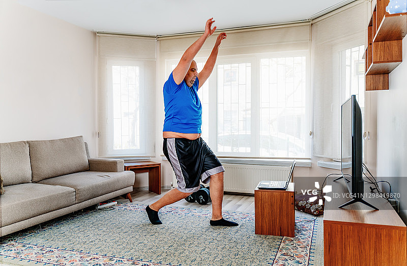 在家一边看笔记本电脑上的教程一边做运动的肥胖男人图片素材