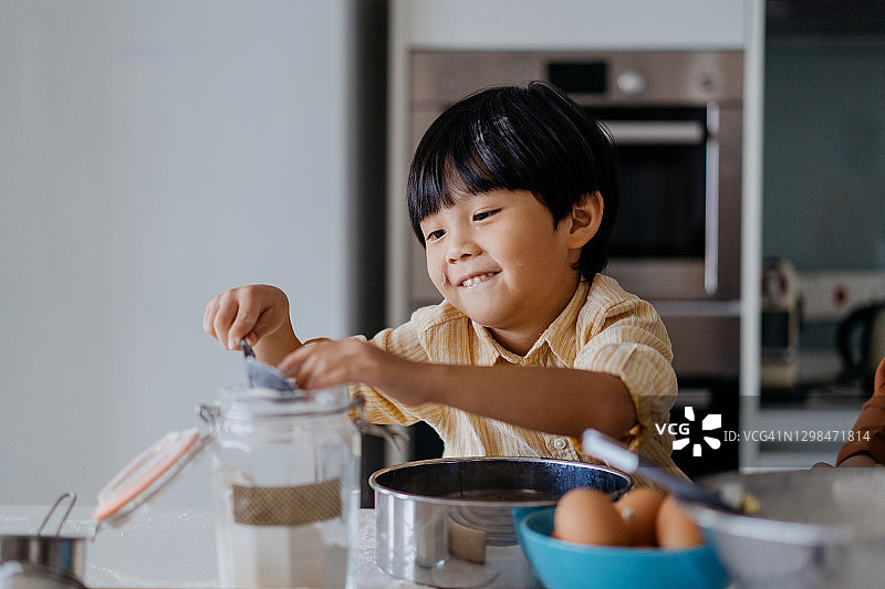 年轻的亚洲男孩在厨房里玩面粉图片素材