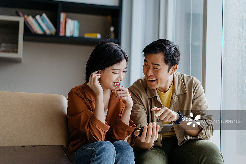 快乐微笑的中国亚洲夫妇一起在智能手机上看节目图片素材