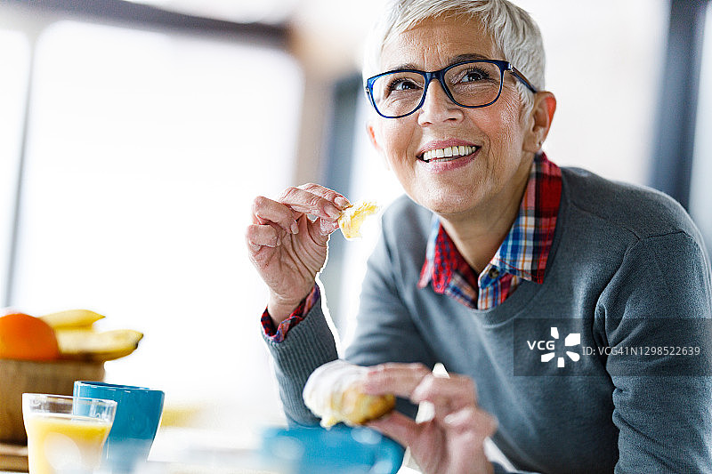 在餐厅里吃羊角面包的快乐中年妇女图片素材