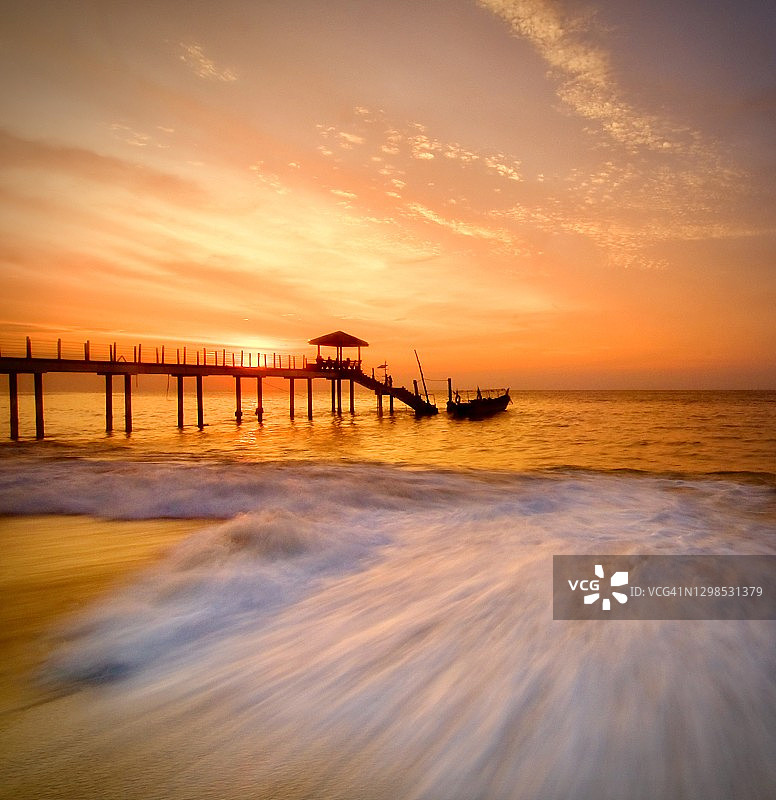 行进波浪、码头和小船的日落图片素材