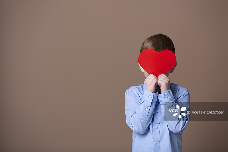 手拿纸质红心并躲藏起来的漂亮男孩图片素材