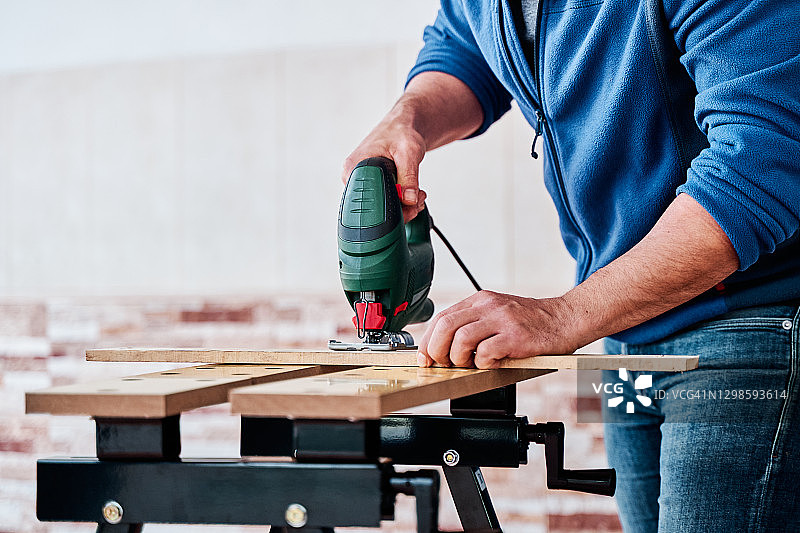 一名身份不明的男人用曲线锯切割木头的细节。在家进行DIY、木工和木匠的概念。图片素材