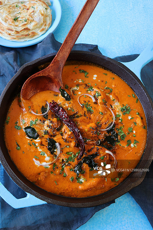 印度黄油鸡/咖喱鸡块图片，盛放在绿松石蓝色的炊具中，里面装满了大块鸡胸肉，咖喱酱汁，并用红洋葱片和芥末籽装饰，拉克哈帕拉塔（分层薄饼）图片素材