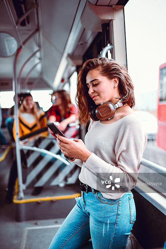 女人戴着耳机和智能手机乘坐公共汽车图片素材