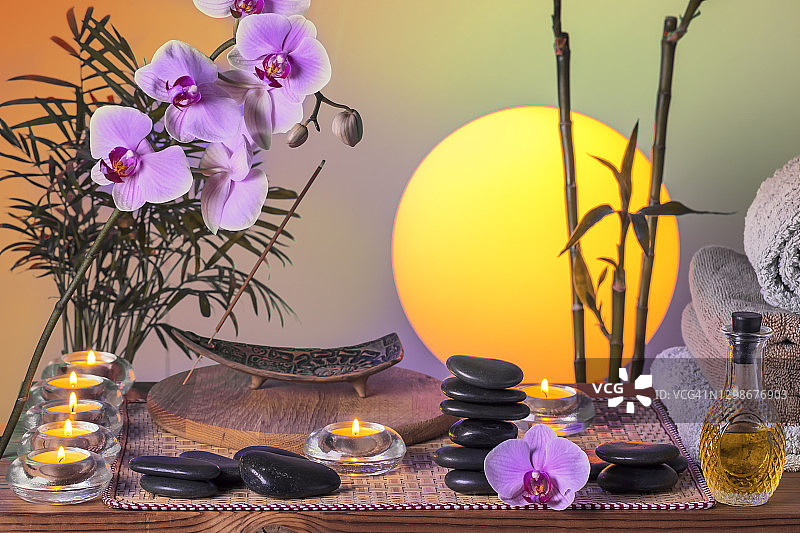 美容Spa概念：黑色按摩石、兰花、竹子、蜡烛、毛巾和按摩油在木桌上图片素材