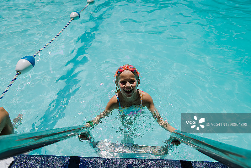 在水中从泳池梯子上向上看的小女孩图片素材