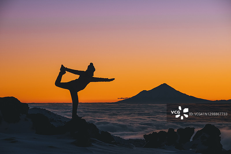 在新西兰汤加里罗国家公园日落时分做瑜伽的年轻女人，背景是塔拉纳基山图片素材