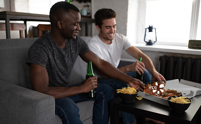 微笑的多元化朋友在足球比赛期间享用披萨和啤酒图片素材