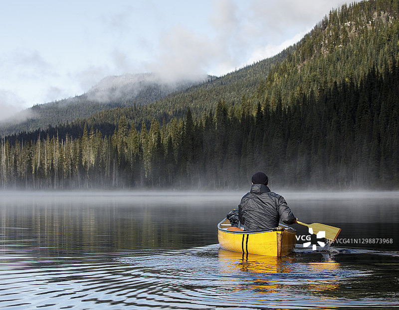 男子在加拿大平静的雾湖上划船图片素材