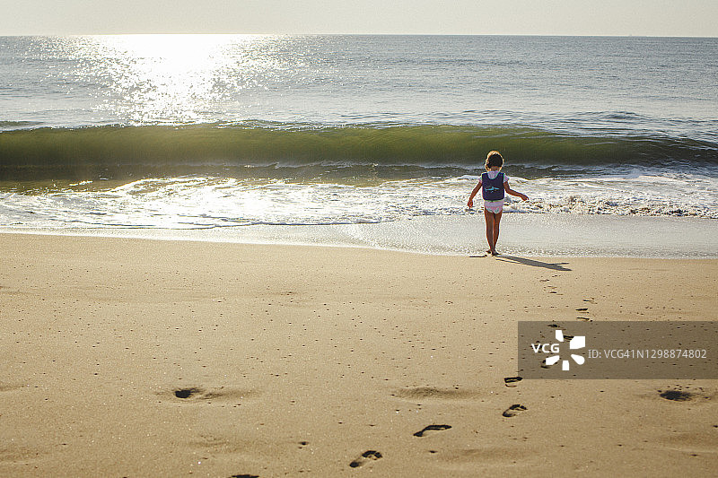 小女孩走过海滩上的金色沙滩走向大海图片素材
