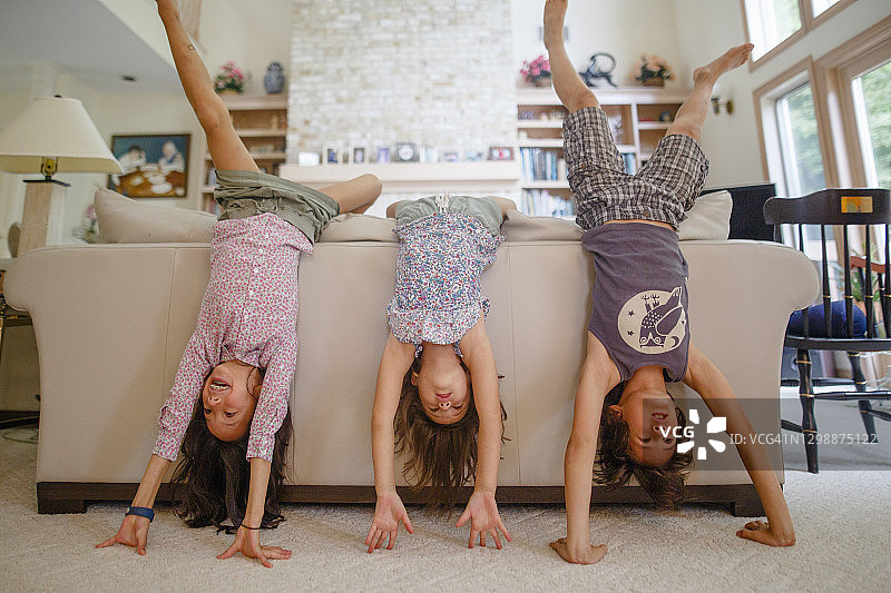 三个孩子在客厅里靠在沙发上倒立图片素材