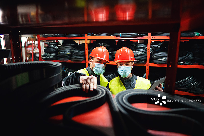 戴着防护口罩的工人在仓库中使用数字平板电脑进行库存控制图片素材