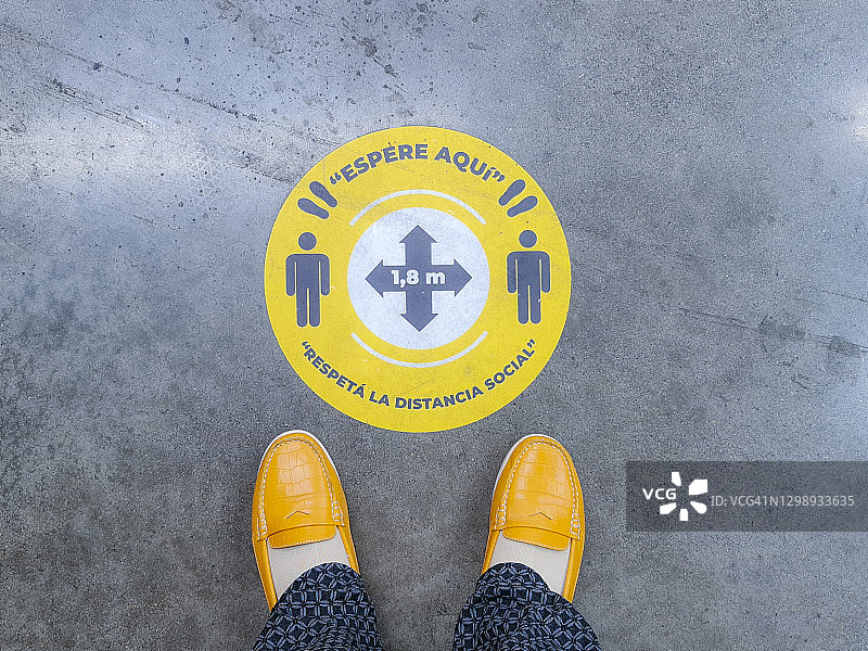 站在新冠疫情期间使用的西班牙语社交距离标志上的人图片素材