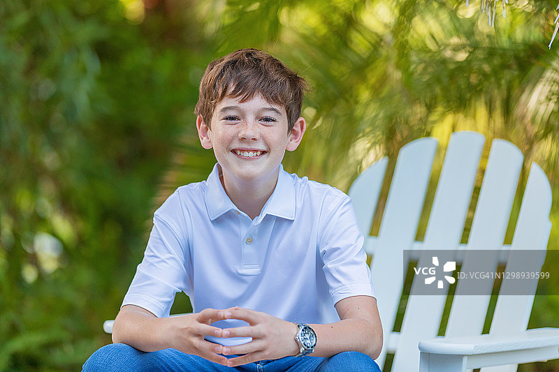 12岁男孩坐在阿迪朗达克椅上，双手合十，面带微笑向前倾图片素材