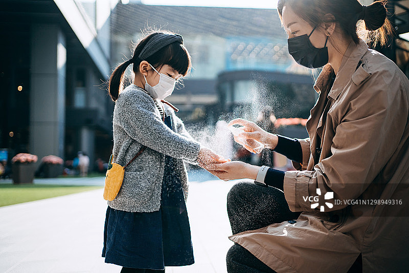 亚洲母亲为女儿户外喷洒免洗洗手液，预防病毒传播。图片素材