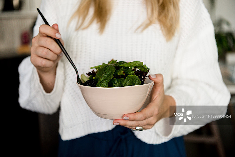 年轻女子在厨房手拿沙拉碗和叉子图片素材