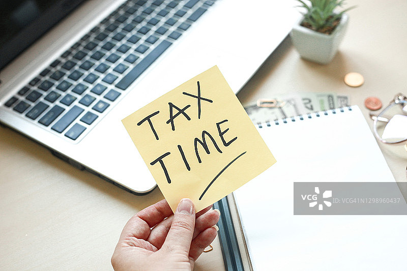 木桌上的记事本、铅笔、笔记本电脑、眼镜、钱和办公用品，税务时间或税务日概念图片素材