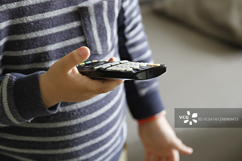 男孩手持遥控器切换电视频道，媒体概念图片素材