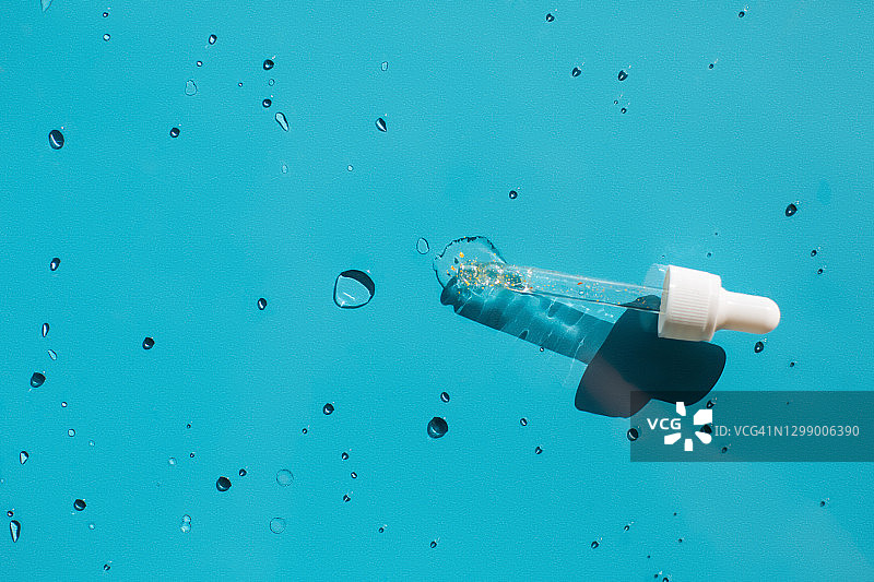 蓝色背景金色闪光天然乳液滴管，年度潮流自护产品图片素材