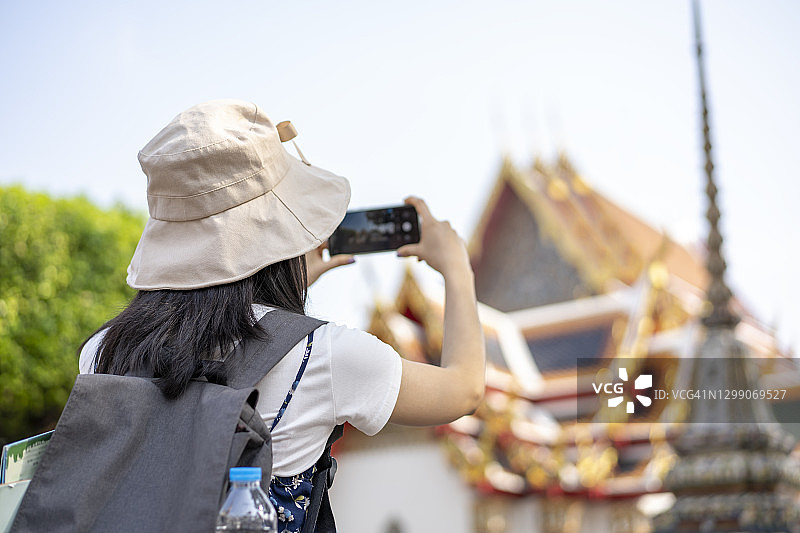 亚洲女游客在泰国曼谷卧佛寺用智能手机拍照。图片素材