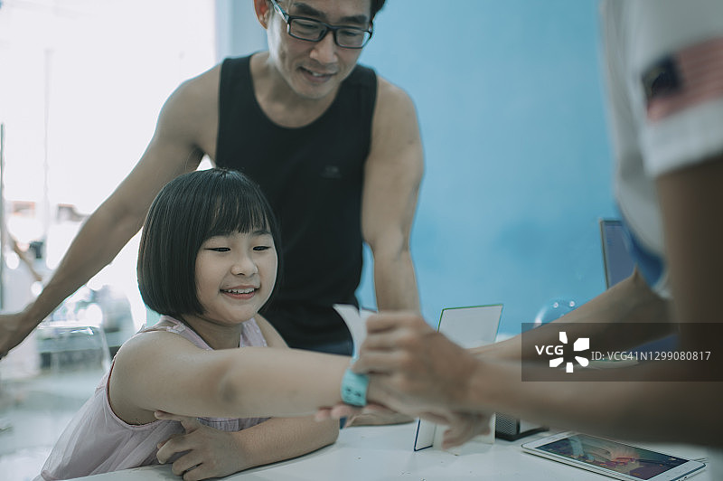 华人年轻女孩让售票员在售票柜台将活动门票腕带戴在她的手臂上，手镯手镯带有贴纸图片素材