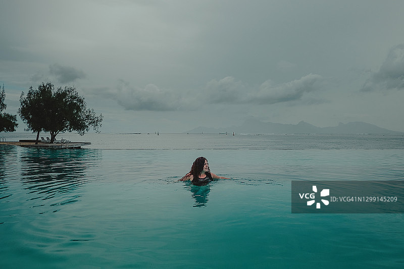无边泳池中的女人，背景是太平洋和云彩图片素材