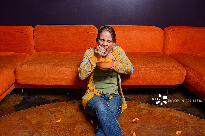 女人坐在地板上，一把一把地吃奶酪泡芙图片素材