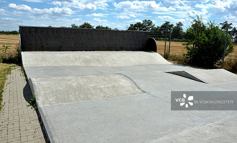 城市郊外带围栏的混凝土滑板运动场。带有栏杆的坡道适合初学者使用滑板车、小轮车和滑板。波浪形区域用于测试跳跃和技巧图片素材