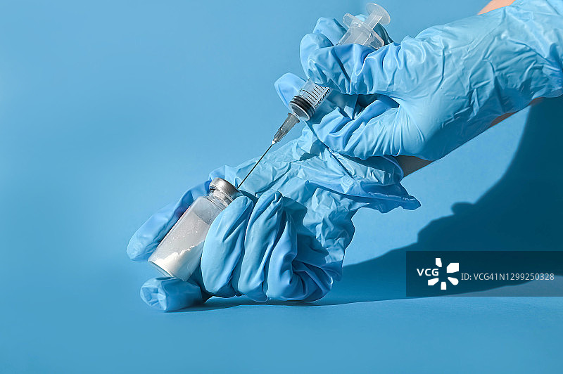 医生戴蓝色手套，在蓝色背景下用药物填充注射器，用于大规模疫苗接种图片素材