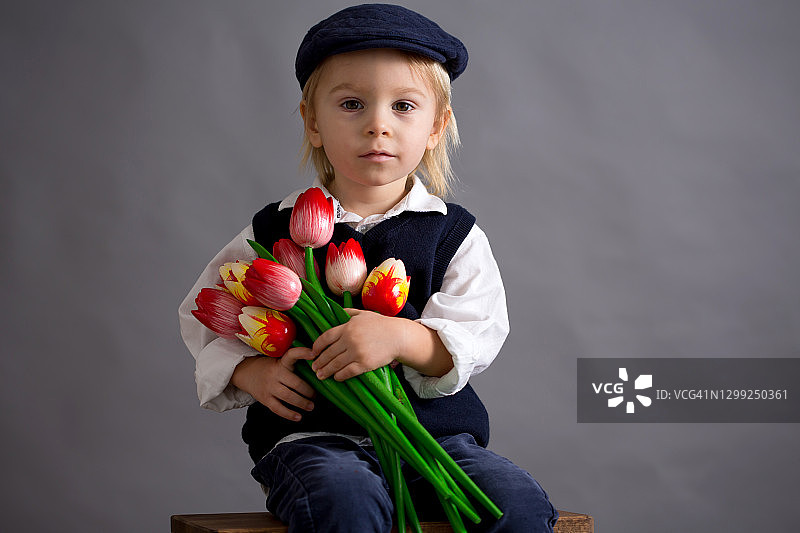 手捧百合花和郁金香的可爱男童，献给母亲节图片素材