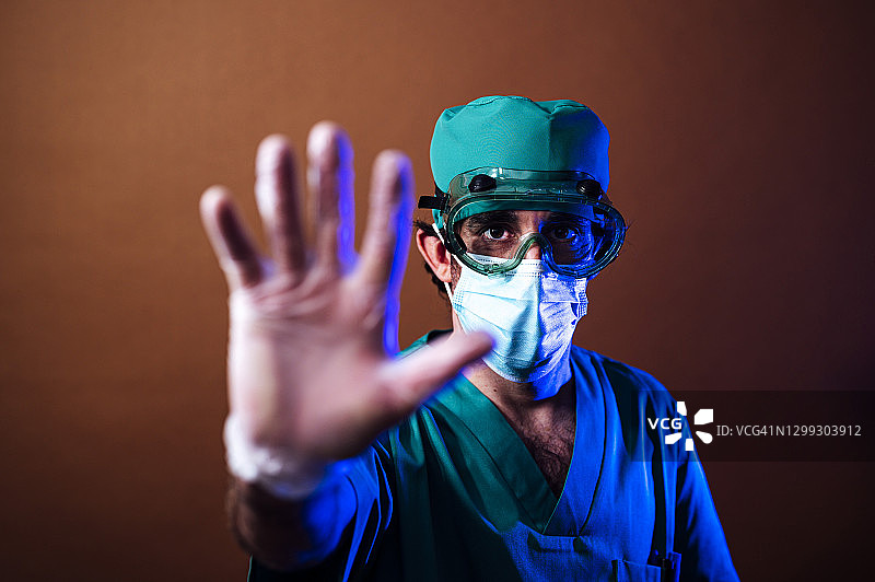 穿着手术服、戴口罩和眼镜的年轻医生在橙色背景下的特写图片素材
