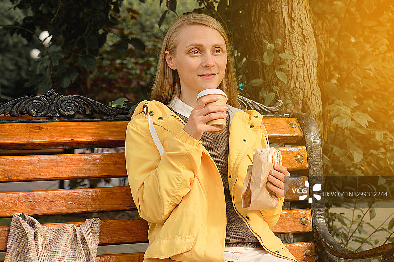 年轻女人在公园长椅上喝咖啡吃烤肉卷饼图片素材