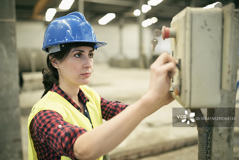 在混凝土工厂启动控制面板的女工。控制按钮和机械的女工图片素材