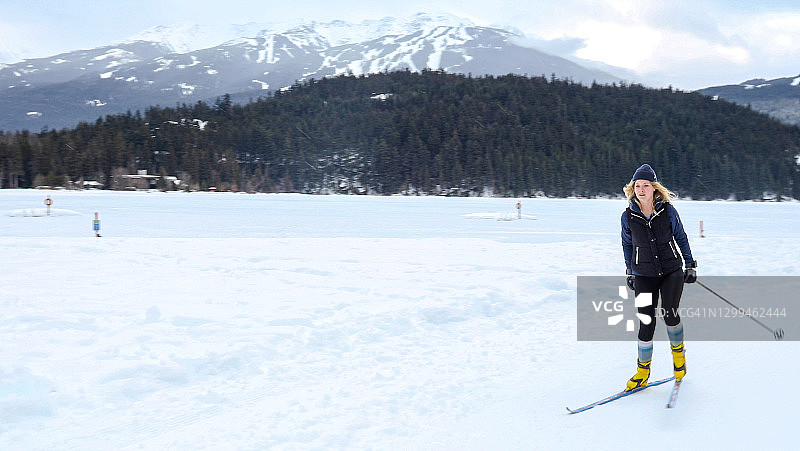 年轻女人在冰冻的湖面上越野滑雪图片素材
