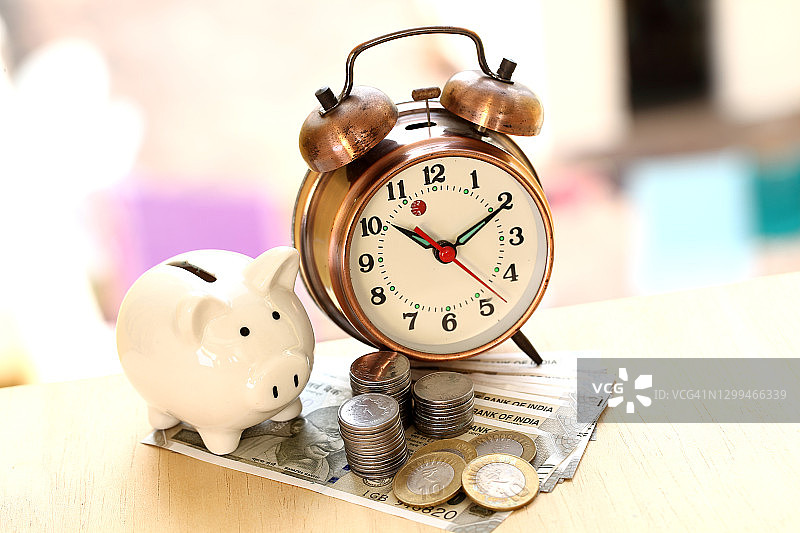 时间和金钱储蓄的概念：小猪存钱罐和印度货币图片素材