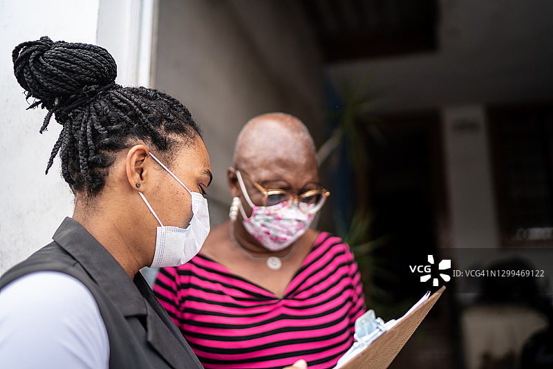 测量员在门口与戴着口罩的老年妇女交谈图片素材