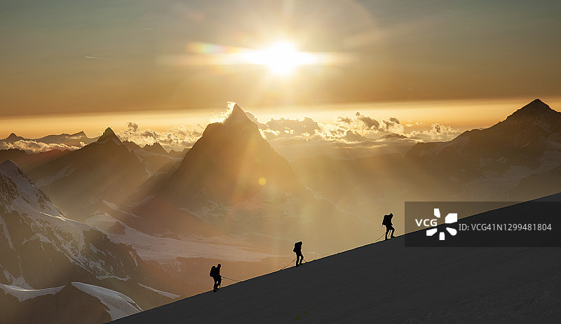 日出时分雪岭上的登山者图片素材