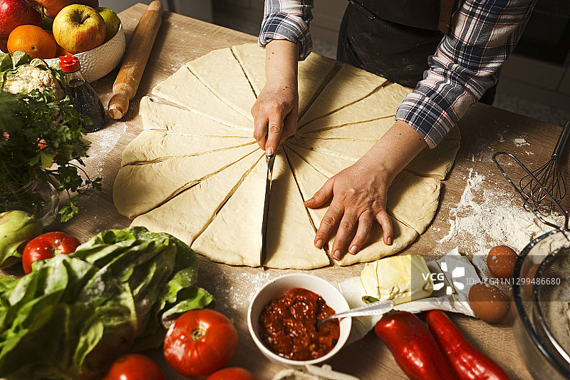 年轻女人制作披萨卷面团并切割形状图片素材