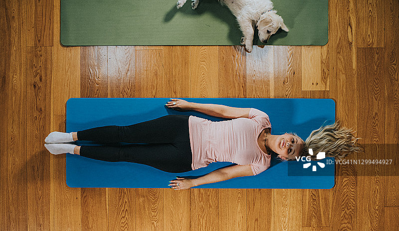 女人和小狗并排躺在瑜伽垫上图片素材