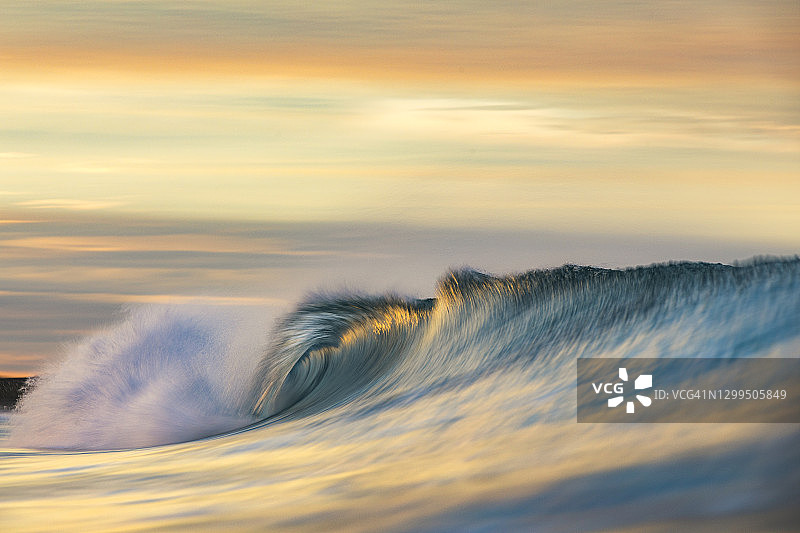 破晓时分，绚丽的橙色和金色光芒照耀着海浪图片素材